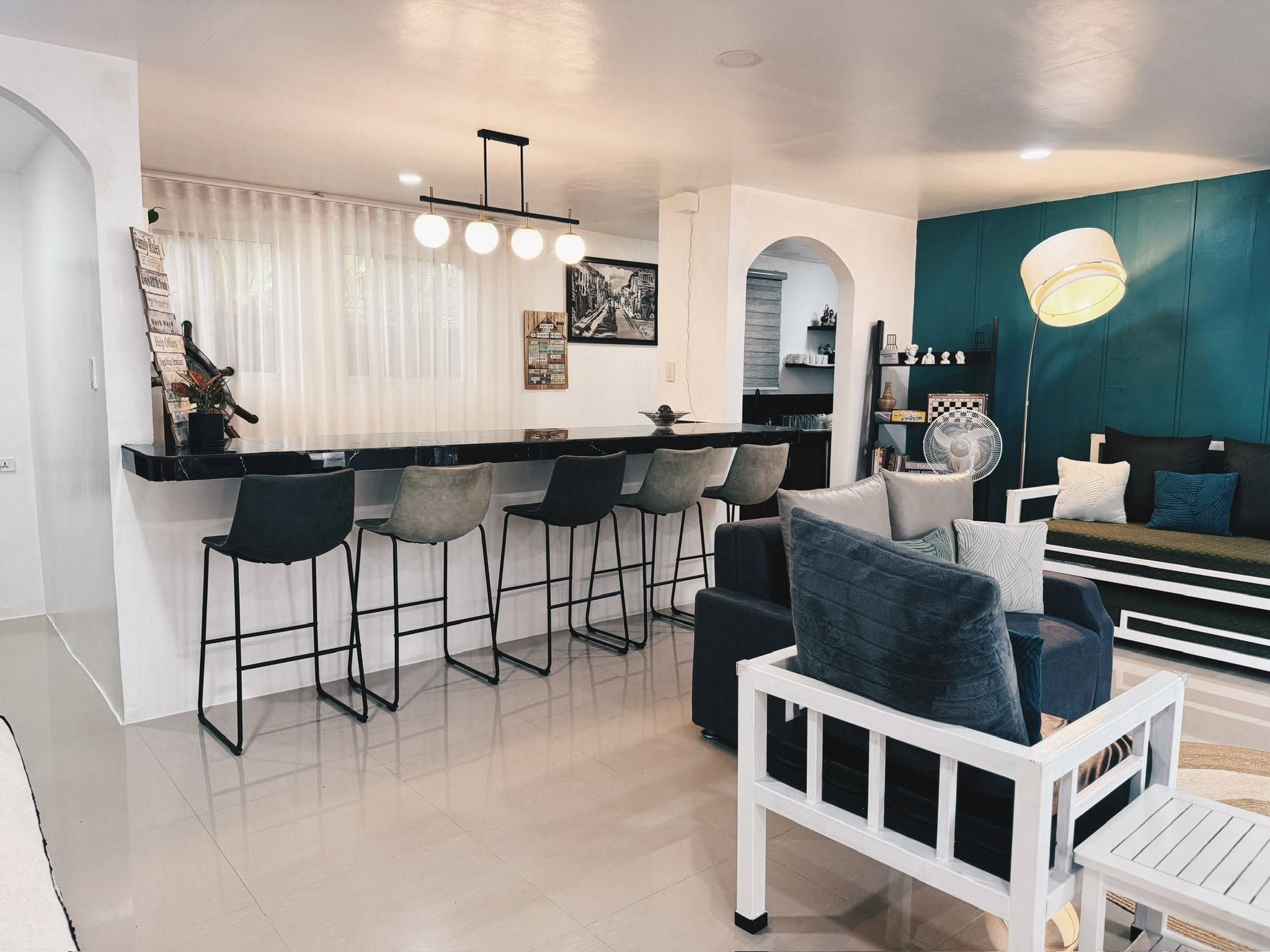 Black marble bar counter with five stools and globe pendant lights, beside a teal feature wall