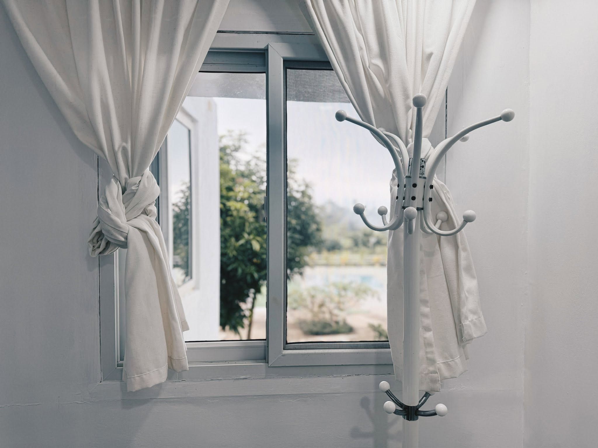 White curtain tied back at a window looking out to the garden and pool