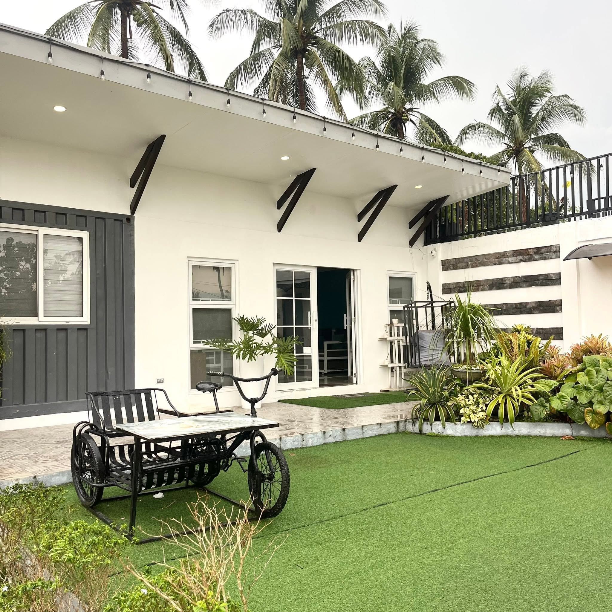 Front of the main house with a turf lawn, a garden bed and a cart-style table in front of the glass doors
