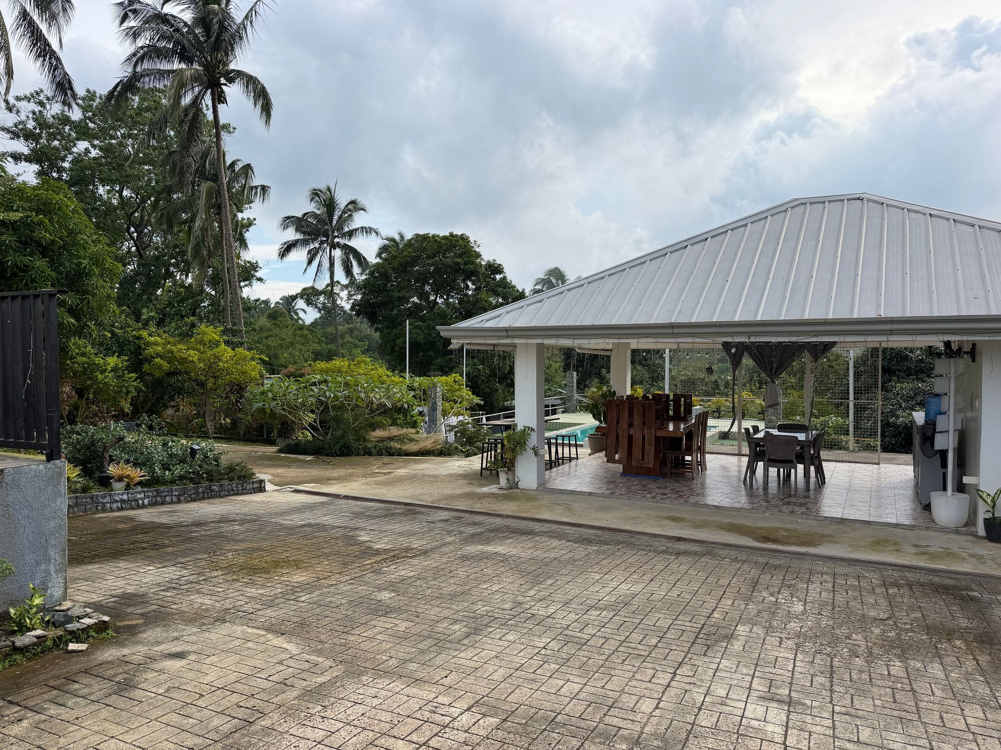 The paved driveway leading to the open-sided pavilion and its dining tables, among palms and garden trees