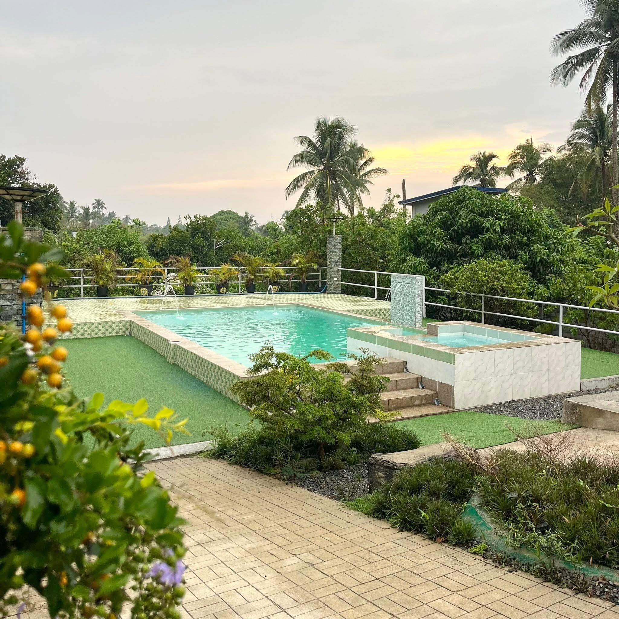 The pool and raised kiddie pool with its small waterfall, turf lawn and potted palms along the railing, in evening light