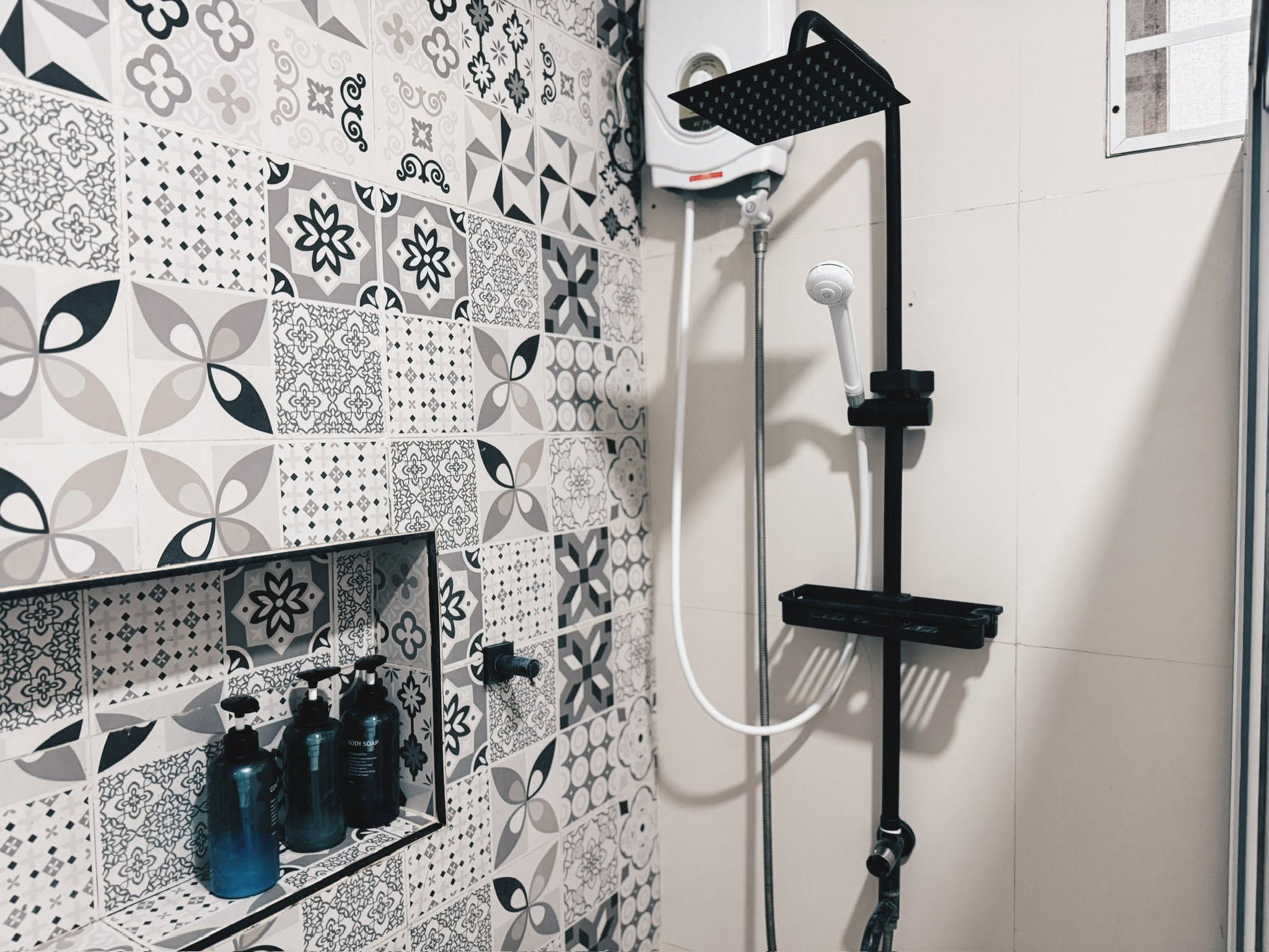Shower with a black rain showerhead, a hand shower and patterned grey tiles with a niche holding bottles